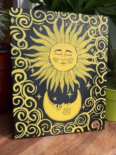 a painting of the sun and moon on a wooden table next to potted plants