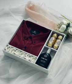 an open gift box containing a red shirt, two bottles of liquor and some white flowers