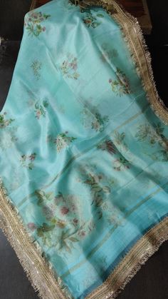 Make a stunning statement with this Teal Pure Organza Silk Saree, beautifully adorned with a vibrant floral digital print that captures the essence of nature. The lightweight organza fabric offers a delicate drape, creating an airy and ethereal silhouette that enhances your elegance. The floral patterns, bursting with rich colors, bring a lively charm to the saree, while the intricate lace trim border adds a touch of sophistication and refinement. Ideal for various occasions, from casual gatherings to festive celebrations, this saree effortlessly combines style and comfort. With its captivating design and luxurious feel, this teal saree is sure to make you stand out in any crowd. Designer Blue Floral Print Dupatta, Festive Floral Print Georgette Digital Prints, Festive Floral Print Digital Prints On Georgette, Designer Tissue Silk Dupatta For Spring, Summer Digital Print Saree, Elegant Summer Saree With Floral Print, Elegant Floral Print Saree For Summer, Elegant Summer Floral Print Saree, Spring Wedding Saree With Floral Print