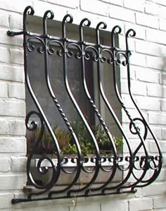 an iron window grill on the side of a white brick building with potted plants in it