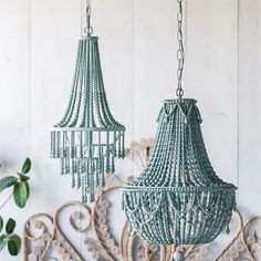 two green beaded chandeliers hanging from hooks on a white wooden wall next to a potted plant