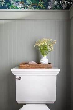 a white toilet sitting in a bathroom next to a wooden tray with flowers on it