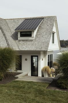 a white house with a black door and windows on the front porch is surrounded by green grass