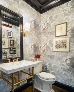 a white toilet sitting next to a bathroom sink under a mirror and framed pictures on the wall