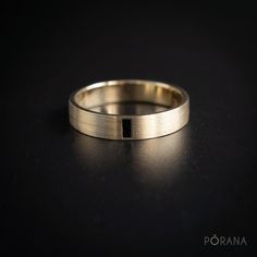 a gold wedding band with a black diamond in the center on a dark surface,