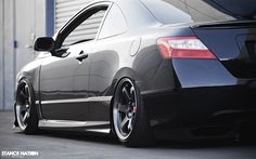 the rear end of a black car parked in front of a building