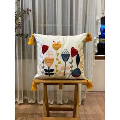 a pillow with flowers on it sitting on a wooden chair in front of a window