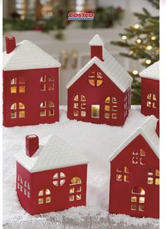 red and white christmas houses sitting on top of snow in front of a christmas tree