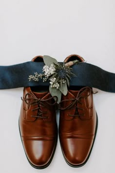 a pair of brown shoes sitting on top of a blue ribbon with flowers in the middle