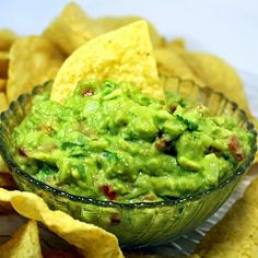 a glass bowl filled with guacamole surrounded by tortilla chips