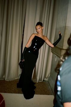 a woman in a black dress standing next to a curtain with her arm extended up