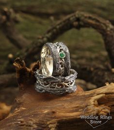 two silver rings with green stones on them sitting on top of a tree branch in the woods