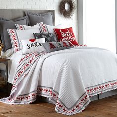 a bed covered in white and red pillows next to a window with christmas decorations on it