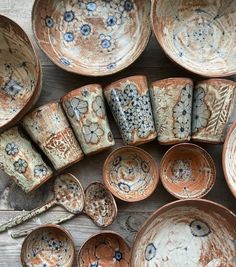 many bowls and spoons are arranged on a table top, including one that has been decorated with blue flowers