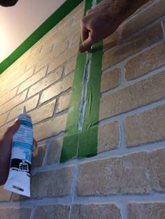 someone is painting a brick wall with green tape and white adhesivement on it