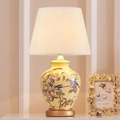 a lamp sitting on top of a white table next to a framed photo and a flowered vase