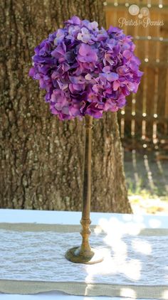 purple hydrangeas are in a brass vase on a white tablecloth under a tree