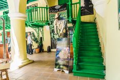 the inside of a building with green staircases and posters on the walls, along with people walking by