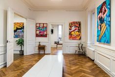 an empty room with paintings on the wall and wooden floors, along with white walls