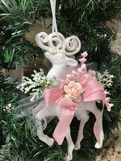 a christmas ornament hanging from a tree with pink ribbon and flowers on it