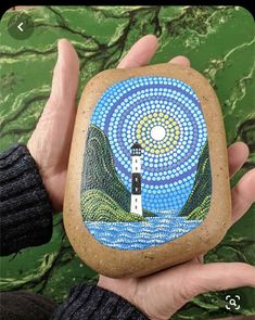 a hand holding a rock with a lighthouse painted on it