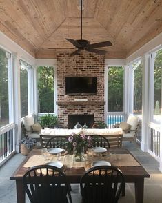 an outdoor living area with couches, table and television on the wall above fireplace