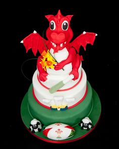 a red dragon is sitting on top of a white and green cake with soccer balls