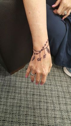 a woman's hand with a tattoo on her left wrist, resting against a chair