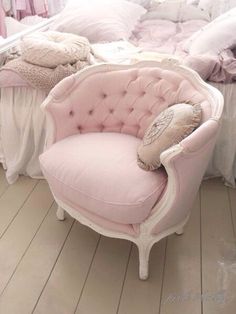 a pink chair sitting on top of a hard wood floor next to a pile of pillows