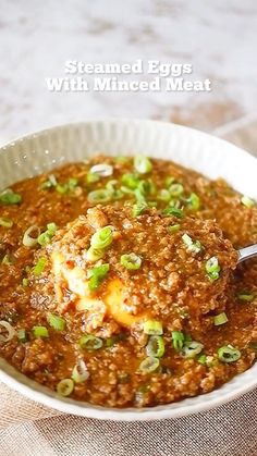 a white bowl filled with meat covered in gravy and topped with green onions