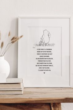 a white vase sitting on top of a wooden table next to a framed print with winnie the pooh