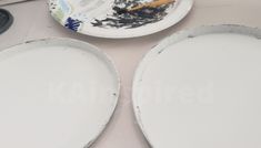 two white plates sitting on top of a table next to a brush and paper plate