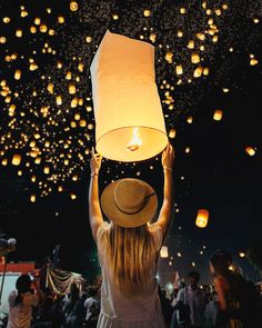 a woman holding up a paper lantern in the air with other lanterns floating above her