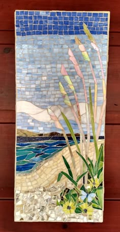 a mosaic tile wall hanging with sea grass and rocks in the sand on a wooden background