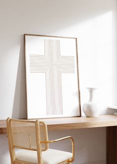 a white vase sitting on top of a wooden desk next to a framed cross poster