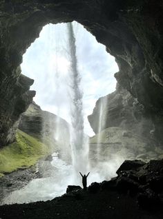 a man standing in front of a waterfall with his arms up and hands raised to the sky