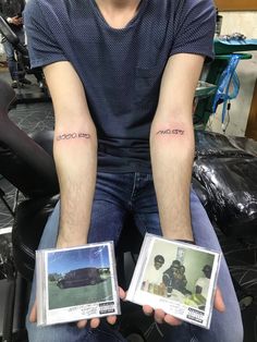 two people with matching tattoos on their arms holding up small photos in front of them