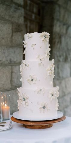 a three tiered white wedding cake with flowers on the side and candles in front