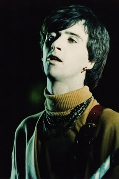 a young man wearing a turtle neck sweater and holding a guitar in his right hand