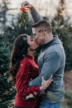 a man and woman kissing in front of a christmas tree with snow falling on them