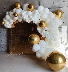 white and gold balloons are hanging on the wall in front of a golden basket with balls