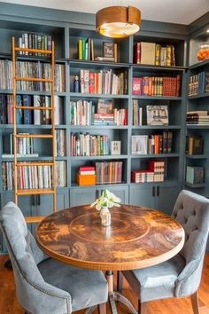 a dining room table with chairs and bookshelves in front of it on the wall