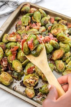 a pan full of brussel sprouts with bacon on top and a wooden spoon