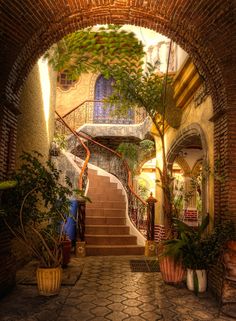 an archway leading to a building with stairs and potted plants