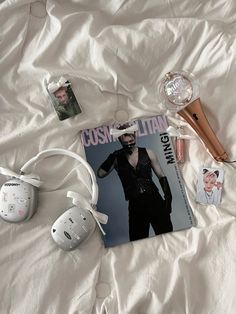 a magazine, headphones, and other items are on a bed with white sheets