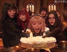 a group of young women standing around a cake with frosting on top of it