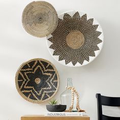 three woven baskets are hanging on the wall above a wooden table with a vase and plant