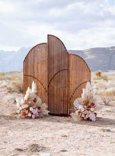 a wooden sculpture in the desert with flowers on it's side and mountains in the background