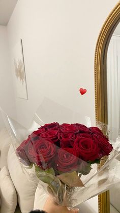 a person holding a bouquet of red roses in front of a mirror with a heart on it