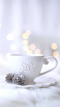 a white cup sitting on top of a bed next to a christmas tree ornament